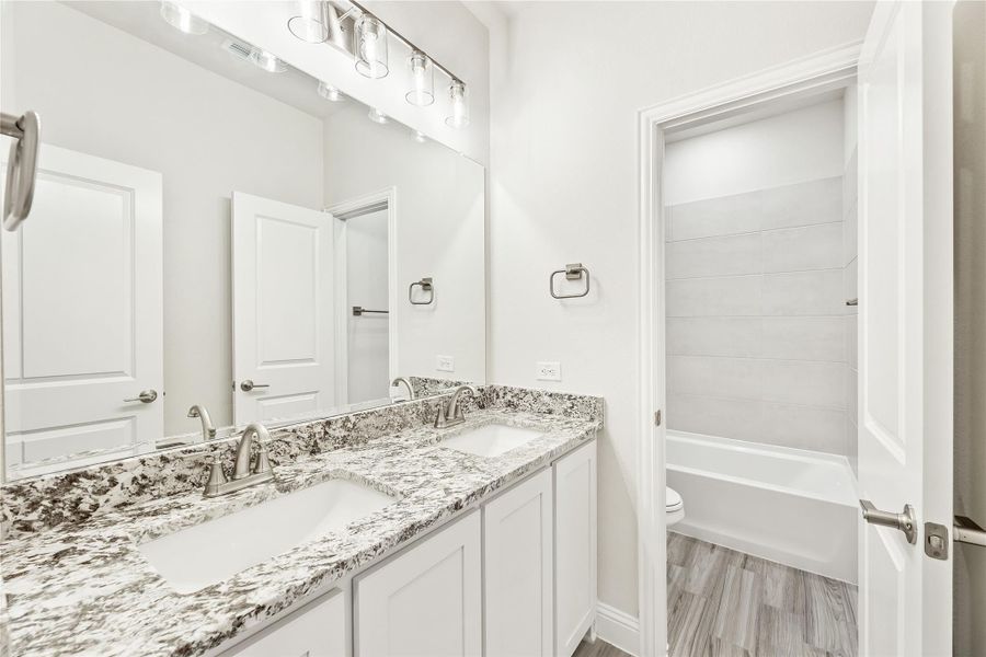 Bathroom with double sink vanity, granite countertops, white cabinets, and separate toilet and tub room