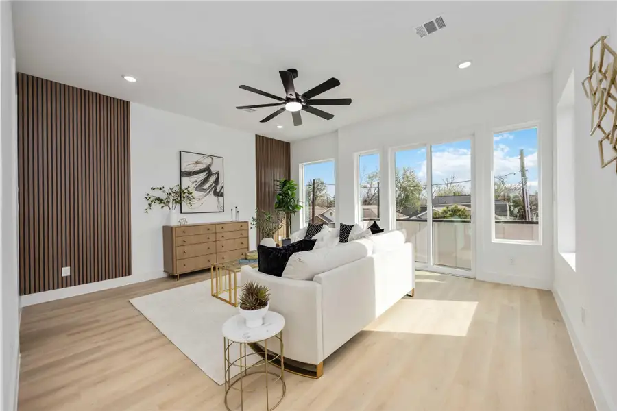 A sun-filled living space featuring modern wood accent walls, sleek finishes, and large windows that invite natural light while offering a seamless balcony connection to the outdoors and fabulous view of the Houston Skyline.
