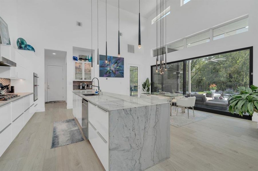 Kitchen featuring white cabinetry, modern cabinets, light stone countertops, and a towering ceiling