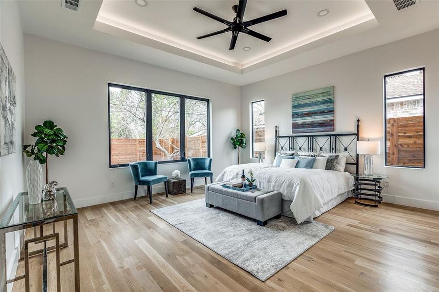 Bedroom with ceiling fan, light wood-type flooring, and a tray ceiling