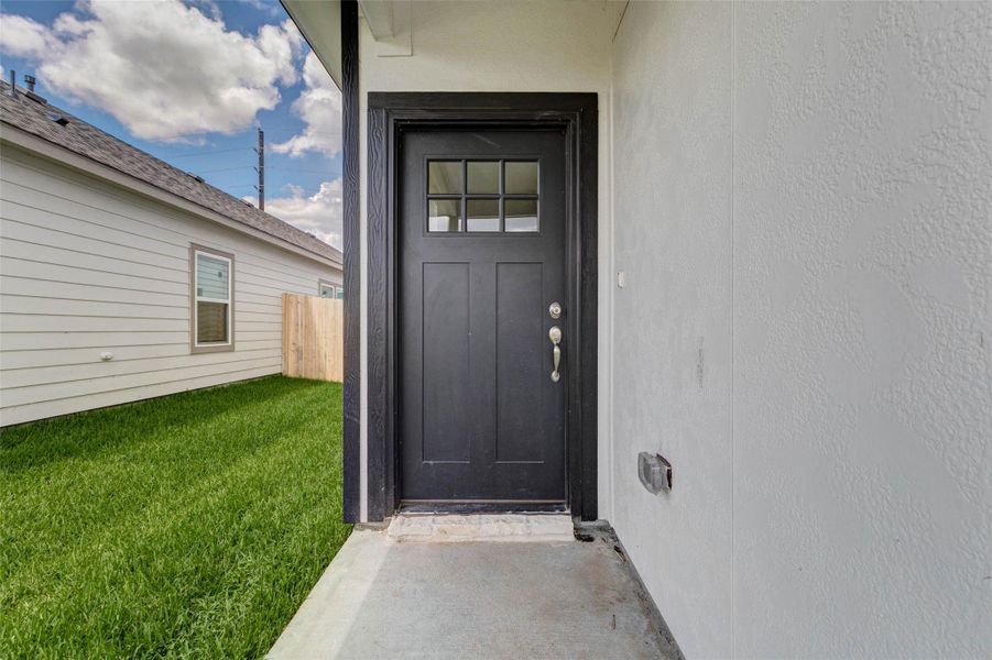 Covered front entry with a black front door, divided-light window detail, neutral exterior walls, and a protected porch area. This inviting entry creates a clean transition from the front yard into the home while adding a touch of modern contrast and character to the exterior.