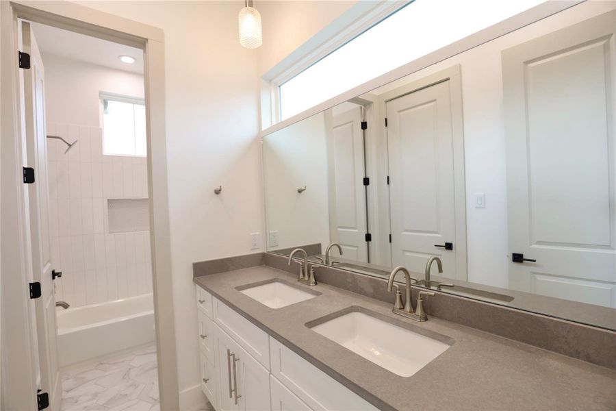 This Jack and Jill bathroom features a custom-sized mirror perfectly completing the space, two sets of drawers, and a specialty imported leather quartz counters. A horizontal window above fills the space with natural light while maintaining privacy. This Jack and Jill bathroom features a custom-sized mirror perfectly completing the space, two sets of drawers, and a specialty imported leather quartz counters. A horizontal window above fills the space with natural light while maintaining privacy.