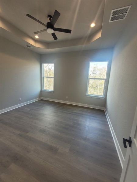 Empty room with a tray ceiling, dark wood finished floors, recessed lighting, and ceiling fan