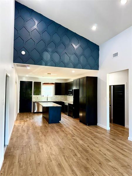 Kitchen featuring appliances with stainless steel finishes, sink, light wood-type flooring, a center island, and a high ceiling