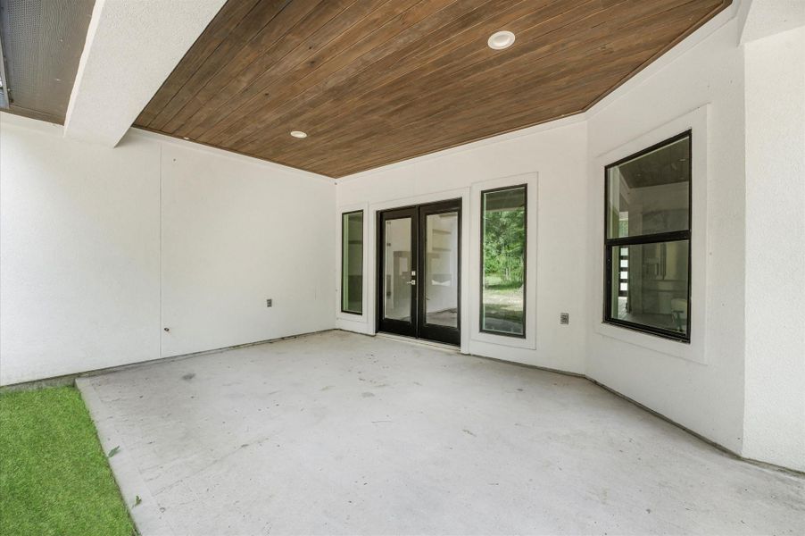 This photo shows a spacious covered patio with a wooden ceiling and recessed lighting. It features large glass doors and windows, opening to a view of greenery. Perfect for outdoor relaxation or entertaining. This photo shows a spacious covered patio with a wooden ceiling and recessed lighting. It features large glass doors and windows, opening to a view of greenery. Perfect for outdoor relaxation or entertaining.