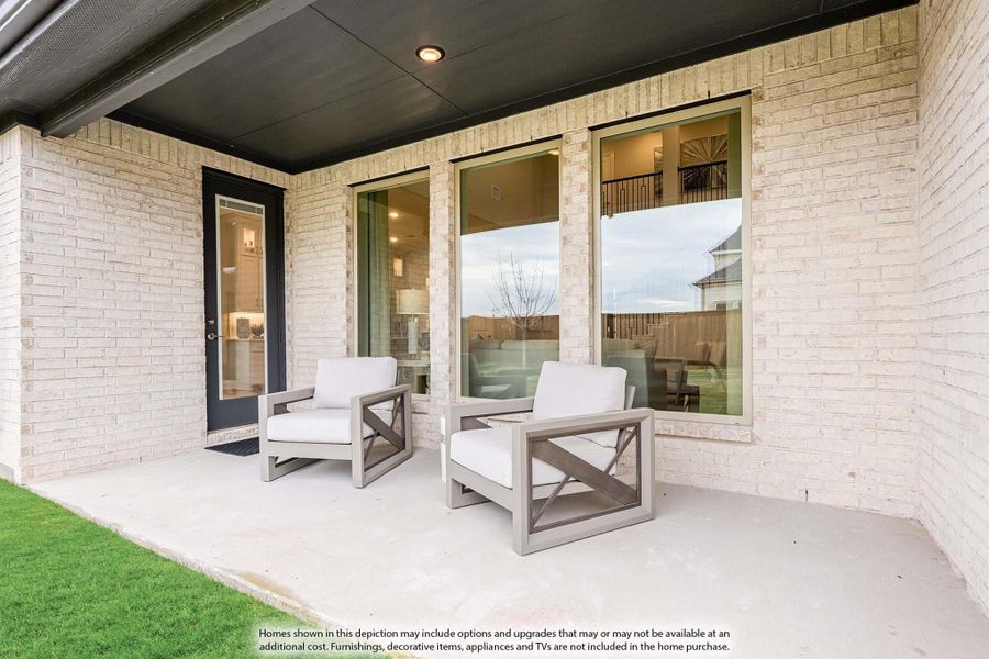 Covered back patio with two white cushion chairs on concrete slab next to brick exterior and large windows