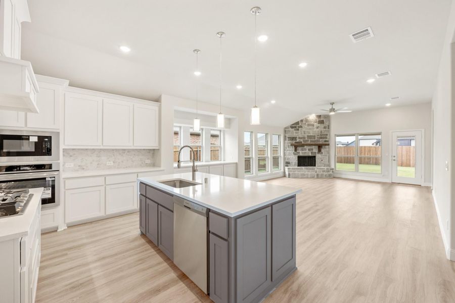 Open-concept kitchen with gray island, white cabinets, and stone fireplace in adjoining living room