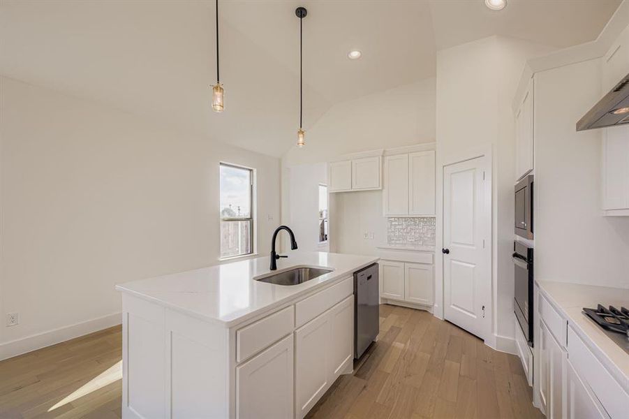 Kitchen featuring lofted ceiling, light wood finished floors, a kitchen island with sink, white cabinets, and recessed lighting Kitchen featuring lofted ceiling, light wood finished floors, a kitchen island with sink, white cabinets, and recessed lighting