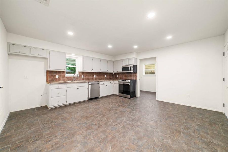 Kitchen with stainless steel appliances, white cabinetry, a sink, and backsplash Kitchen with stainless steel appliances, white cabinetry, a sink, and backsplash