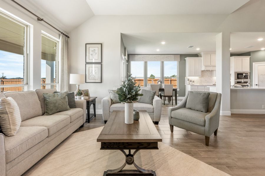 Open-concept living room with neutral furniture, wood-look floors, and kitchen visible in background