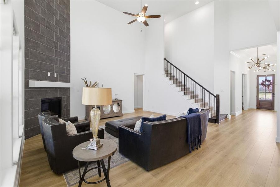 Two-story living area featuring a dark tile fireplace with a white mantel, light wood-finish flooring, a contemporary chandelier, and a staircase with dark wood handrails and black metal balusters