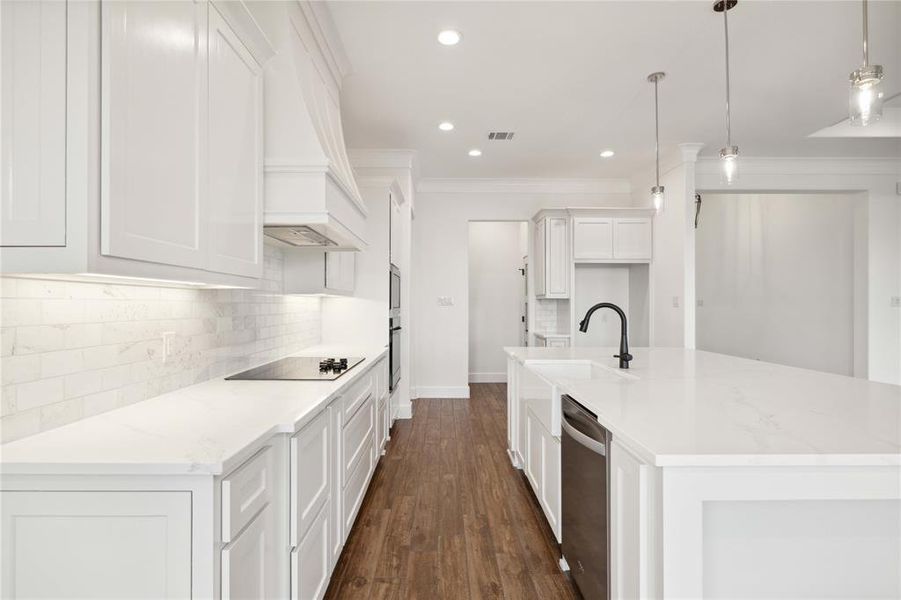 Kitchen featuring light stone countertops, dark hardwood / wood-style flooring, black electric cooktop, pendant lighting, and a kitchen island with sink