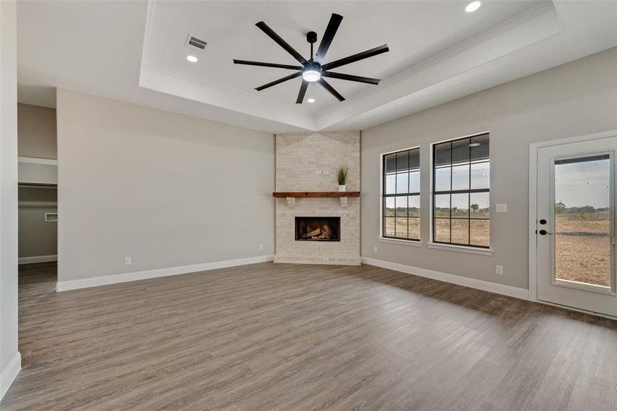 Unfurnished living room with a large fireplace, ornamental molding, a tray ceiling, ceiling fan, and hardwood / wood-style flooring