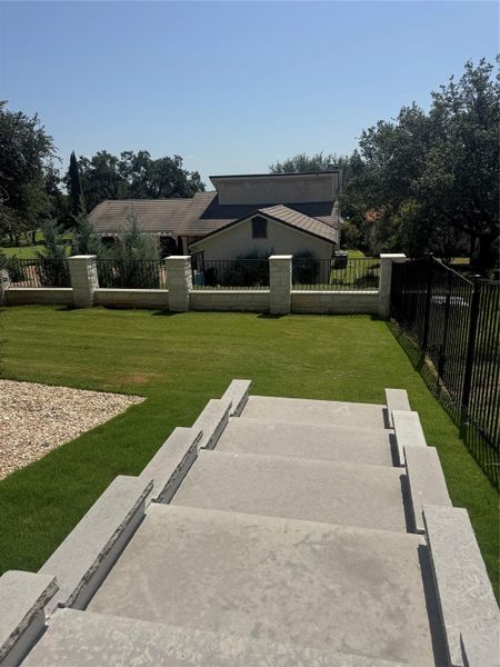 Concrete steps descend to a meticulously landscaped lawn, framed by an elegant stone and wrought iron fence.