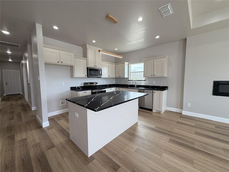 Kitchen featuring a kitchen island, stainless steel appliances, white cabinets, light wood-style flooring, and recessed lighting