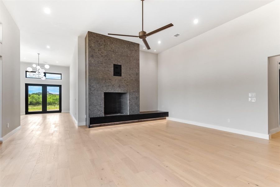 Unfurnished living room with a high ceiling, ceiling fan, light wood-type flooring, recessed lighting, and a tile fireplace Unfurnished living room with a high ceiling, ceiling fan, light wood-type flooring, recessed lighting, and a tile fireplace