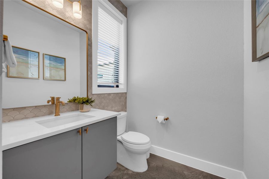Half bathroom: vanity featuring a gold-framed mirror, contemporary lighting, and a white countertop with an integrated sink