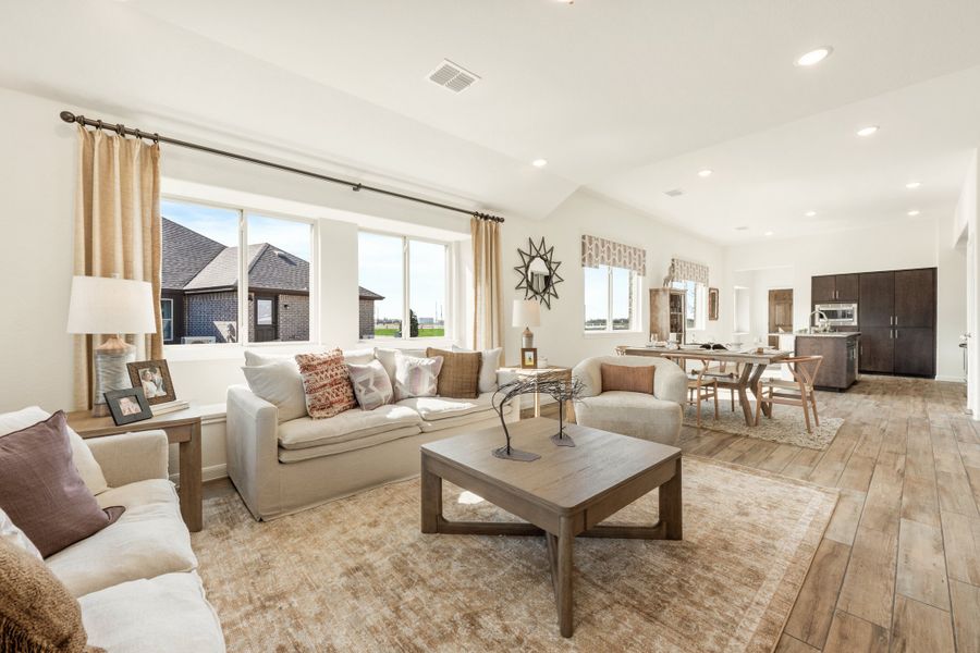 Open-concept living room with vaulted ceiling, wood-look floors, and dining area visible in background