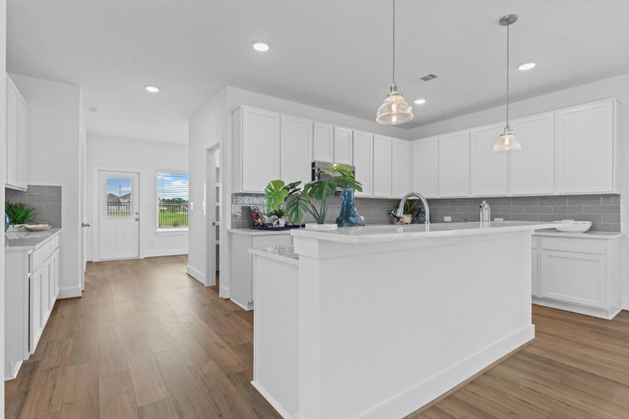 Entry into the kitchen reveals an open-concept design with continuous flooring, pendant lighting, and a thoughtful layout that flows into the living and dining areas for easy entertaining. **Image Representative of Plan Only and May Vary as Built**.