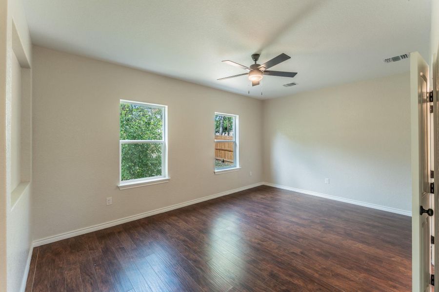 Spacious room featuring wood-finish flooring, two windows, a ceiling fan with integrated lighting, and neutral wall tones