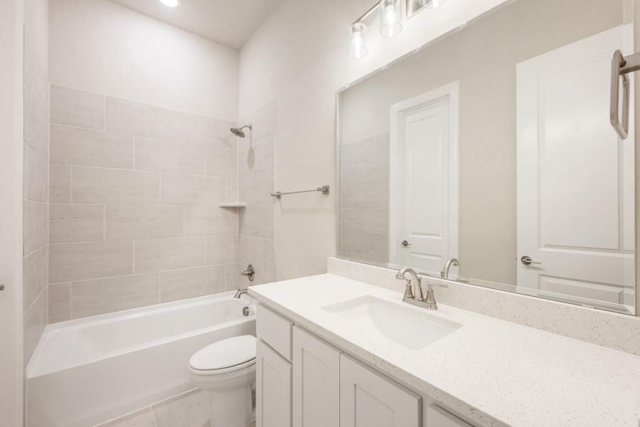 Bathroom with white quartz vanity, large mirror, and tiled tub-shower combo with brushed nickel fixtures