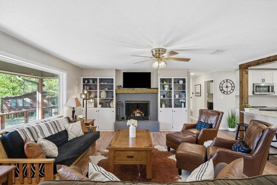 Living space featuring wood-finish flooring, a fireplace with a dark stone surround, custom built-in shelving, and large window with lake views