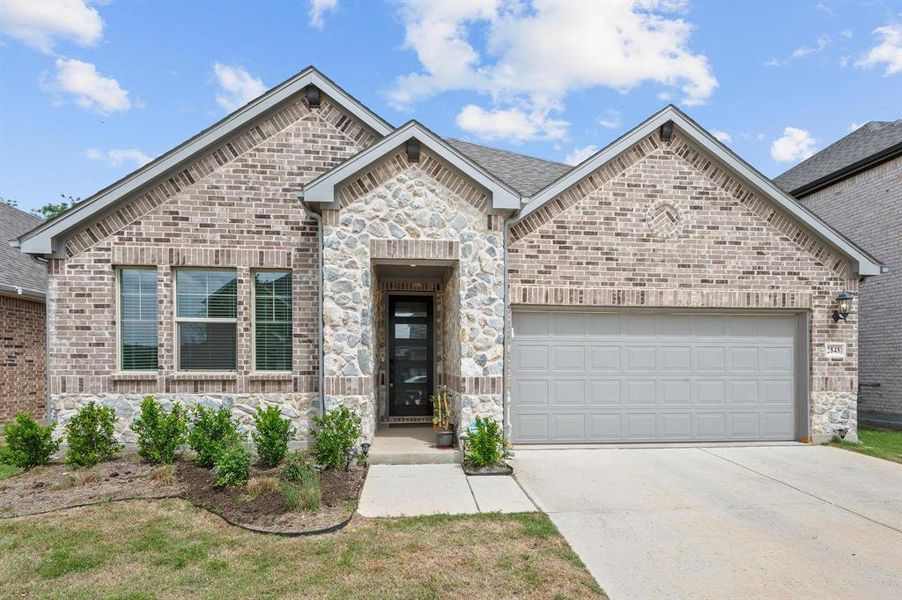 Brick and stone façade featuring a covered entry, multiple window styles, an attached two-car garage, and a concrete driveway Brick and stone façade featuring a covered entry, multiple window styles, an attached two-car garage, and a concrete driveway