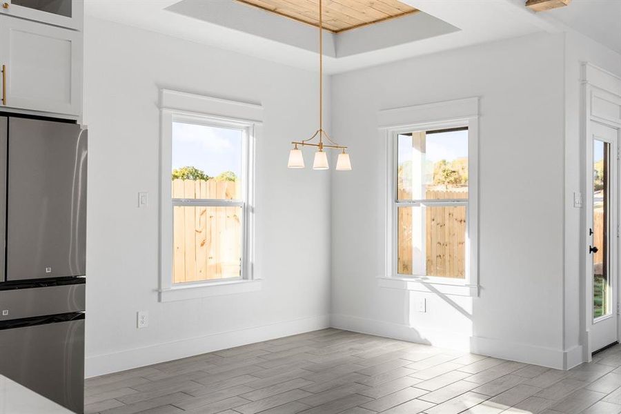 Unfurnished dining area featuring light hardwood / wood-style floors, wooden ceiling, a wealth of natural light, and a tray ceiling