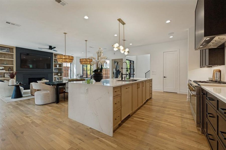 Open-concept kitchen featuring a waterfall island with a white stone countertop, light wood-finish cabinetry, and contemporary pendant lighting Open-concept kitchen featuring a waterfall island with a white stone countertop, light wood-finish cabinetry, and contemporary pendant lighting