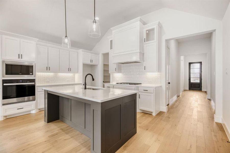 Kitchen with stainless steel appliances, two tone color scheme, light wood-style flooring, decorative light fixtures, and a center island with sink