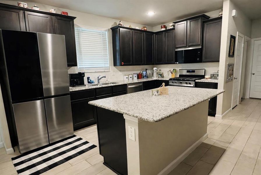 Kitchen with stainless steel appliances, a center island, light stone countertops, dark cabinetry, and recessed lighting