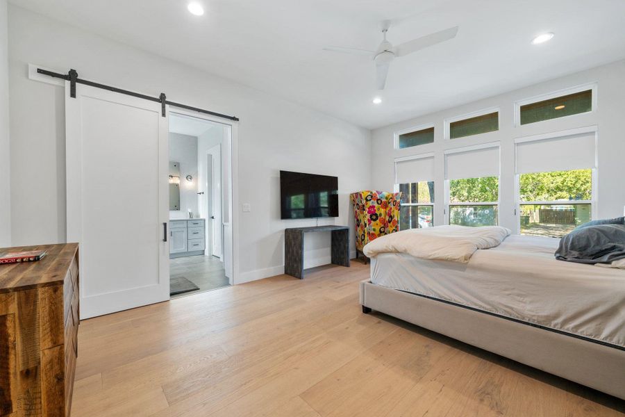 Bedroom with light wood finished floors, a barn door, recessed lighting, ceiling fan, and ensuite bath
