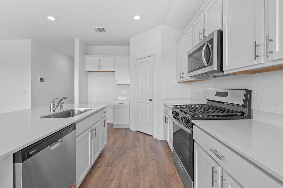 Kitchen with stainless steel appliances, recessed lighting, dark wood finished floors, white cabinets, and light stone counters