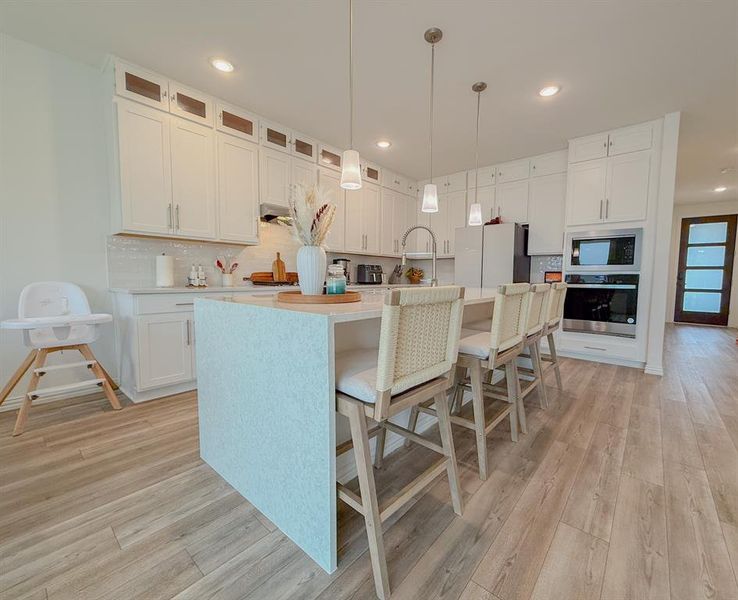 Kitchen with decorative backsplash, freestanding refrigerator, built in microwave, light wood-style floors, and stainless steel oven