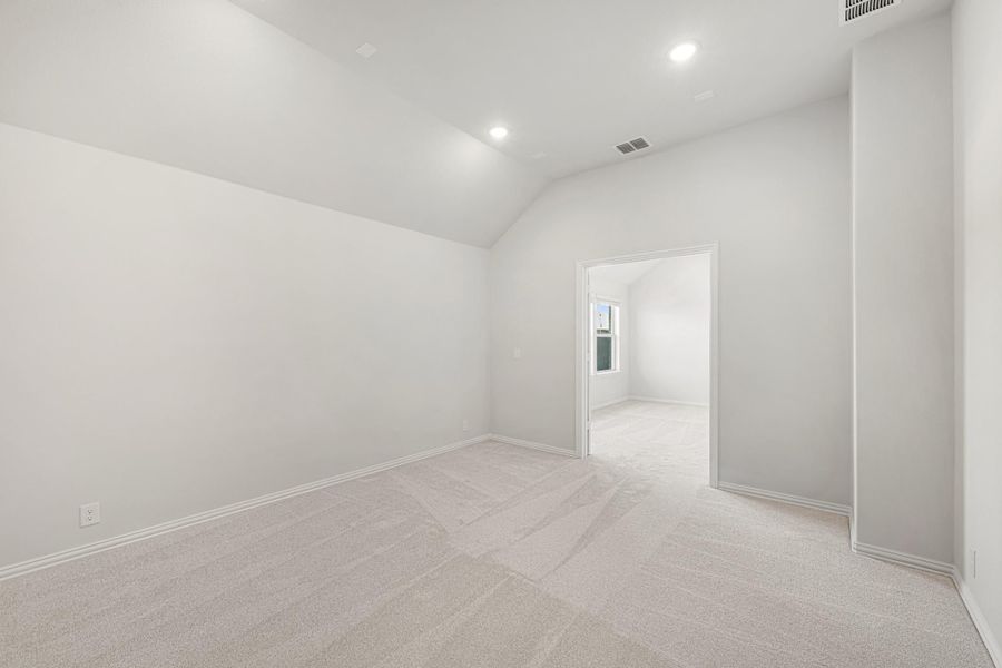 Empty bedroom with vaulted ceiling, recessed lighting, and light carpet flooring