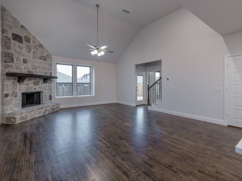 Unfurnished living room featuring dark hardwood / wood-style floors, ceiling fan, lofted ceiling, and a stone fireplace