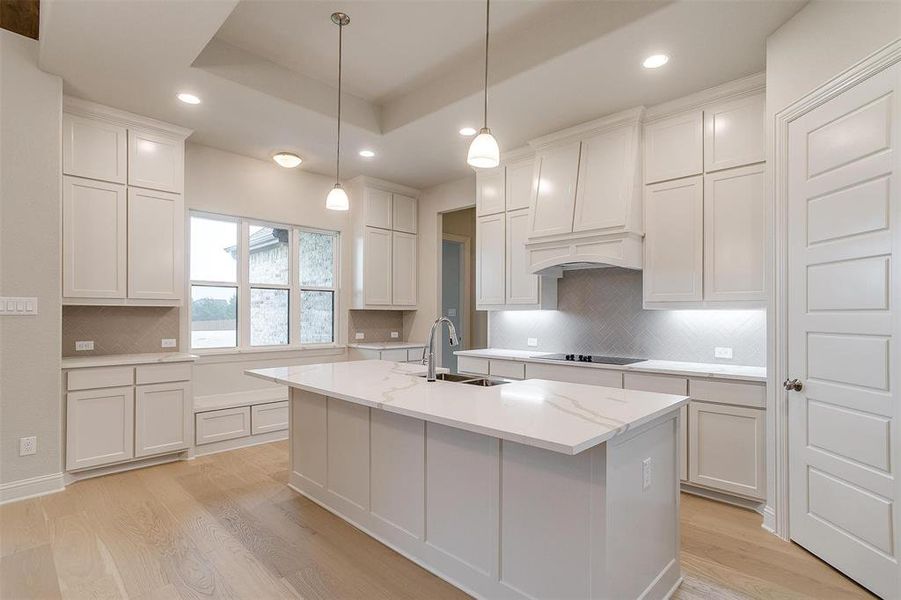 Kitchen featuring light wood-type flooring, white cabinets, sink, decorative backsplash, and a center island with sink