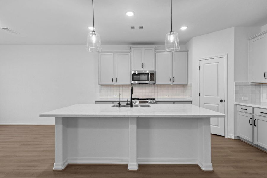 This light and bright kitchen features a large quartz island, white cabinets, a large sink overlooking your family room, recessed lighting, and beautiful backsplash.