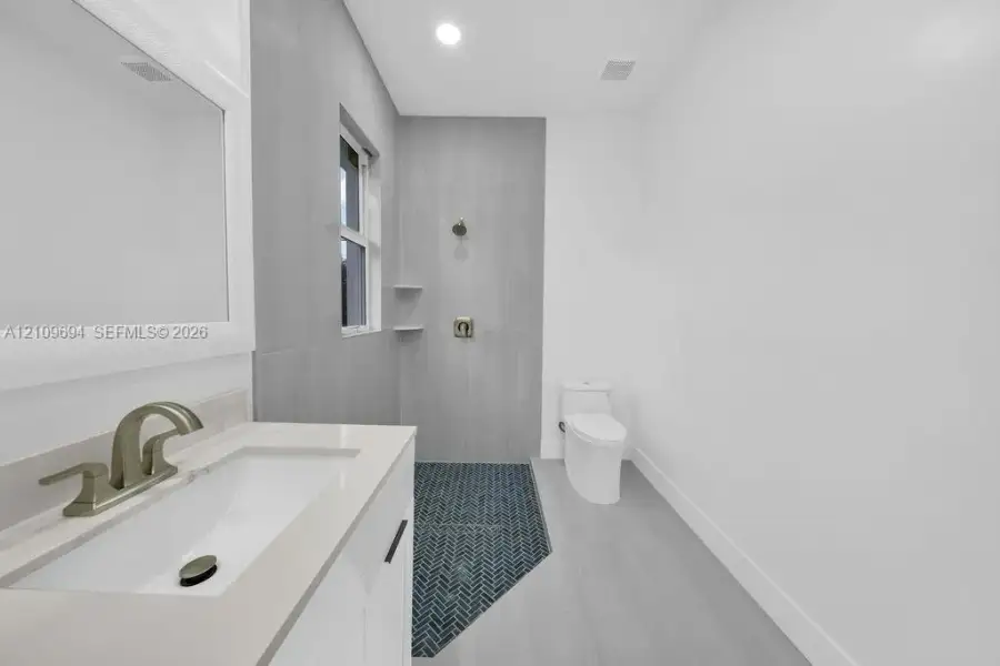 Bathroom featuring a white vanity with quartz countertop, under-mount sink, brushed-finish faucet, shower with grey large-format wall tile, and navy blue herringbone floor tile