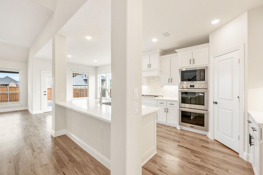 Kitchen with white cabinets, stainless steel double oven, and light wood floors open to living area