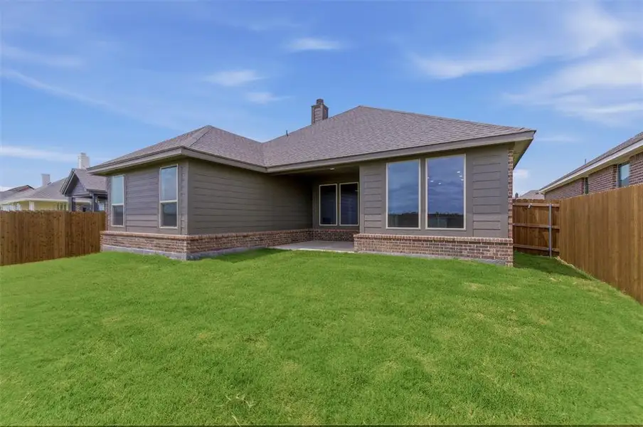 Expansive backyard featuring a manicured lawn, wood fencing, and a covered patio area