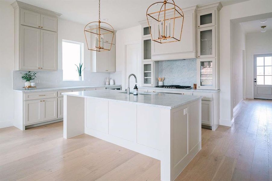 Kitchen featuring tasteful backsplash, a kitchen island with sink, sink, pendant lighting, and an inviting chandelier