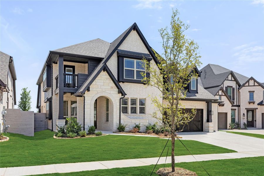Two-story home with cream brick exterior, dark trim, arched entry, and two-car garage on a corner lot with green lawn Two-story home with cream brick exterior, dark trim, arched entry, and two-car garage on a corner lot with green lawn