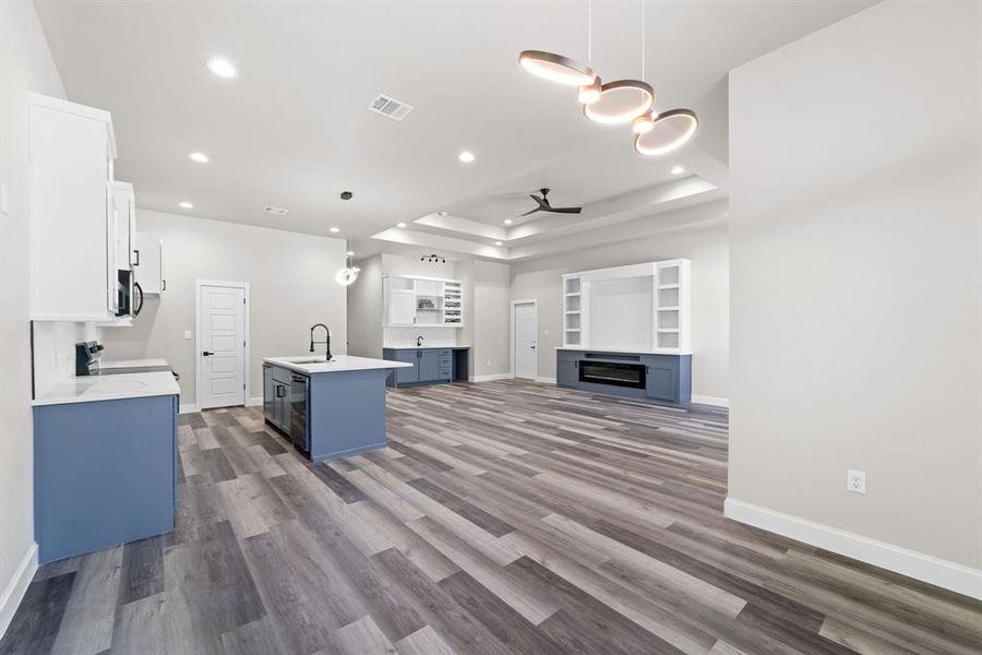 Kitchen featuring blue cabinetry, dark hardwood / wood-style floors, decorative light fixtures, an island with sink, and white cabinetry