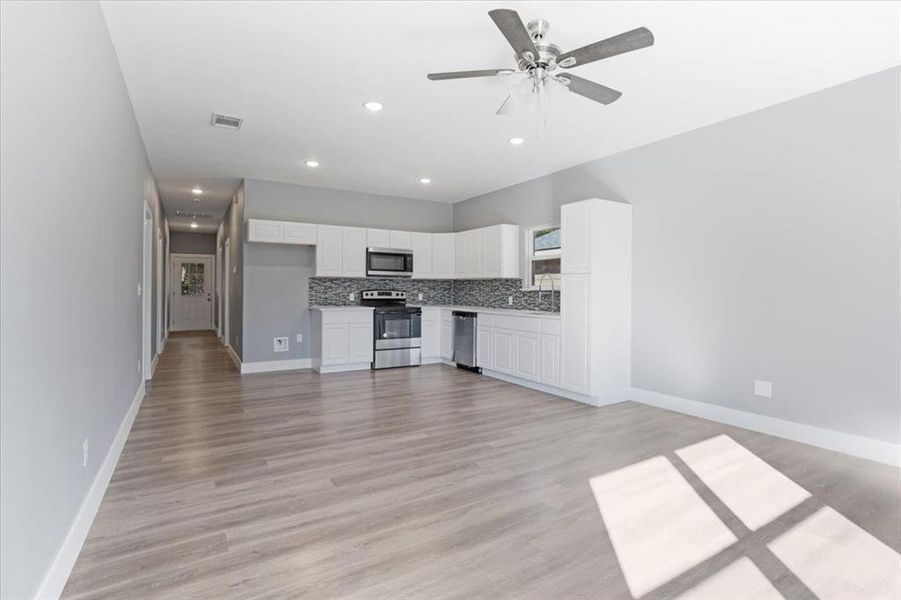 Kitchen featuring light hardwood / wood-style floors, white cabinets, backsplash, appliances with stainless steel finishes, and ceiling fan