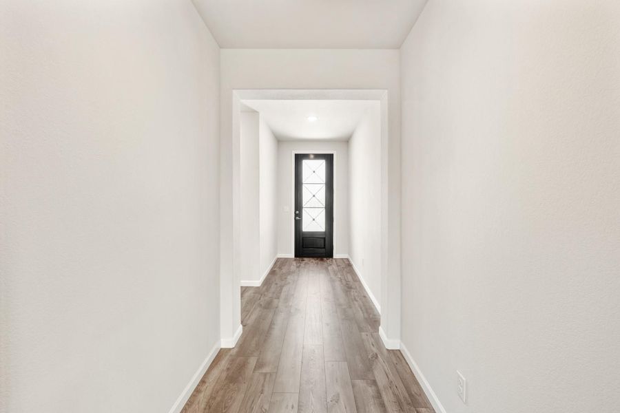 Narrow entryway hallway with wood-look floors, white walls, and black front door with glass panel