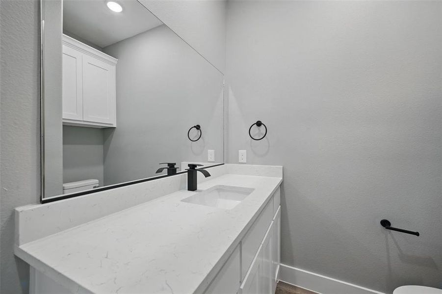Half bathroom with toilet, baseboards, vanity, and wood finished floors