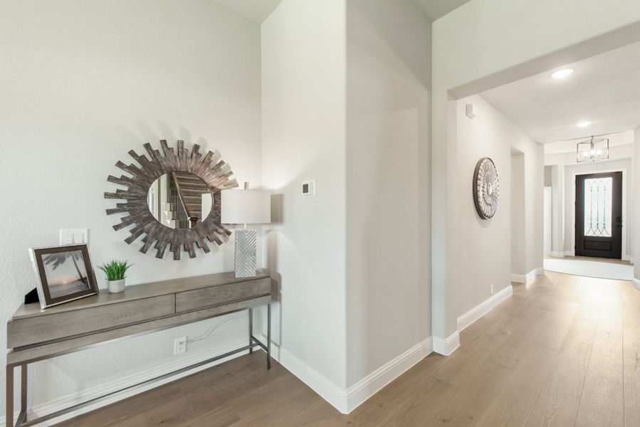 Entryway hallway with wood floors, console table, sunburst mirror, and dark front door visible at end of hall