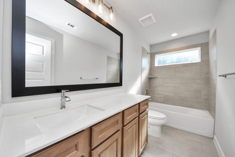 Secondary bath features tile flooring, bath/shower combo with tile surround, light stained wood cabinets, beautiful light countertop.