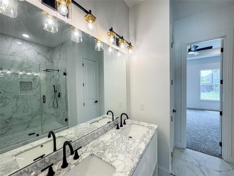 Full bath featuring marble look tile flooring, a marble finish shower, double vanity, a ceiling fan, and baseboards Full bath featuring marble look tile flooring, a marble finish shower, double vanity, a ceiling fan, and baseboards